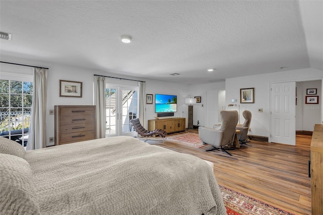 bedroom with wood-type flooring, access to outside, and a textured ceiling