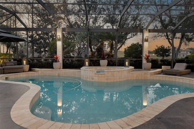 pool at dusk featuring an in ground hot tub and a lanai