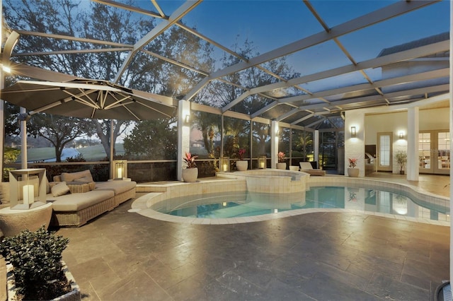 pool at dusk with an in ground hot tub, outdoor lounge area, glass enclosure, and a patio