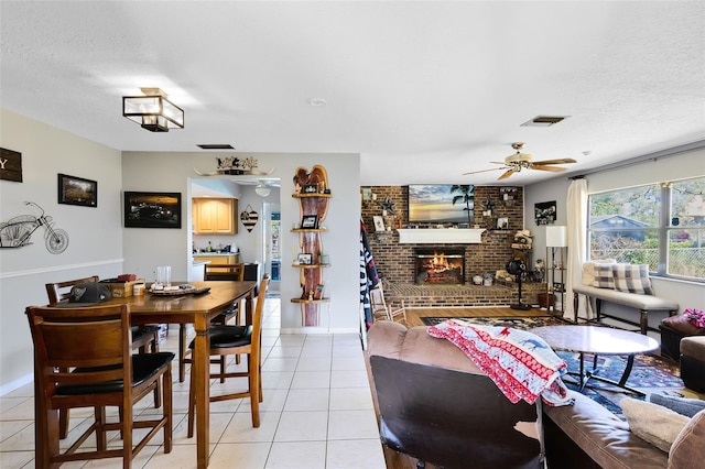 tiled dining room with ceiling fan, a brick fireplace, and a textured ceiling