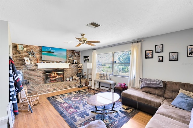 living room featuring ceiling fan, wood-type flooring, a fireplace, and a textured ceiling