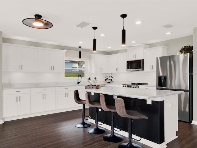 kitchen with dark wood-type flooring, white cabinetry, hanging light fixtures, appliances with stainless steel finishes, and a kitchen island