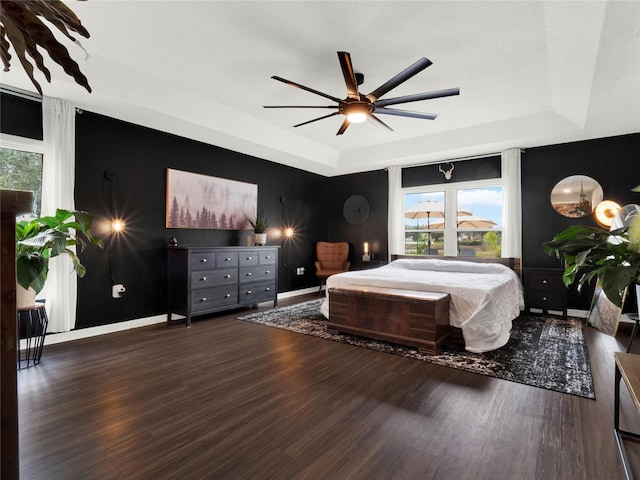 bedroom with dark hardwood / wood-style flooring, a raised ceiling, and ceiling fan