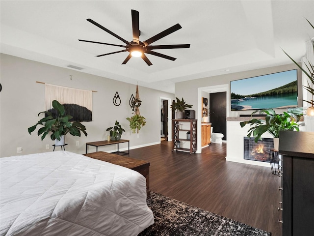 bedroom with dark hardwood / wood-style floors, ceiling fan, and a tray ceiling