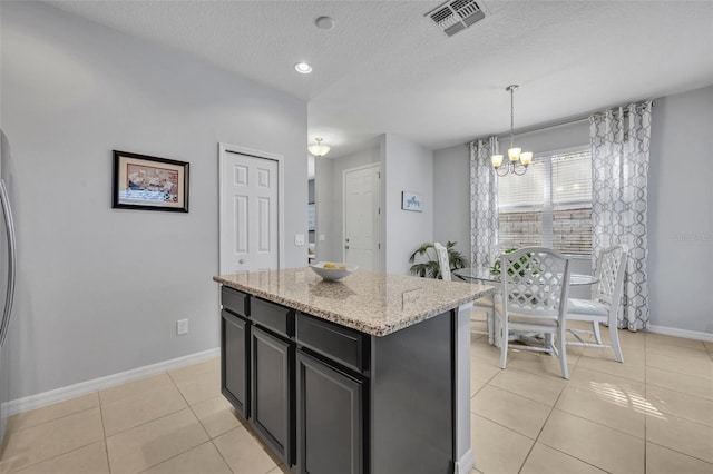 kitchen featuring pendant lighting, a kitchen island, light stone counters, a textured ceiling, and light tile patterned flooring