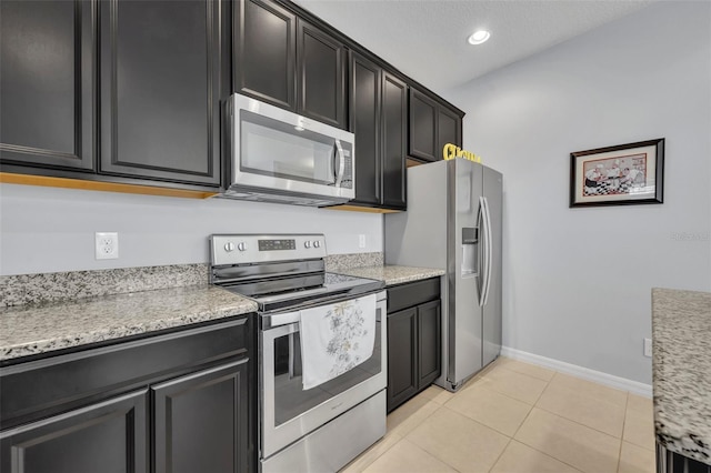 kitchen featuring appliances with stainless steel finishes, light tile patterned floors, a textured ceiling, and light stone counters