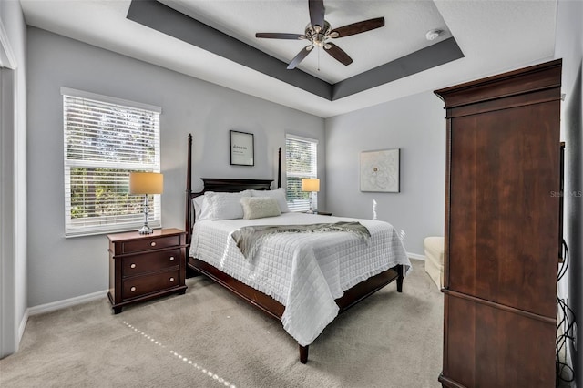 bedroom with ceiling fan, a tray ceiling, and light carpet