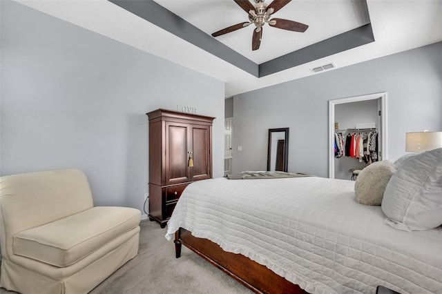 bedroom featuring ceiling fan, a tray ceiling, light carpet, a walk in closet, and a closet