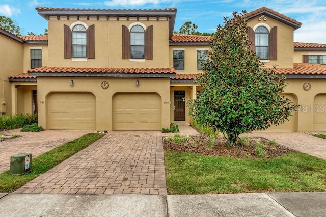 mediterranean / spanish house featuring a garage, decorative driveway, and stucco siding