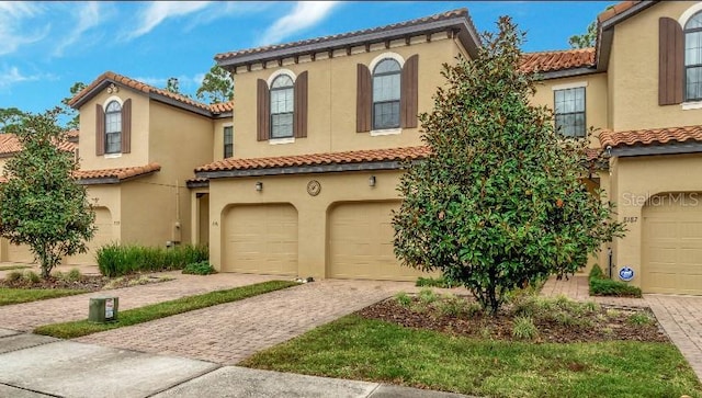 mediterranean / spanish-style house featuring a garage, a tiled roof, decorative driveway, and stucco siding