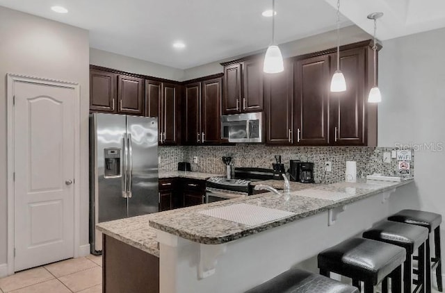 kitchen with stainless steel appliances, hanging light fixtures, a peninsula, and light stone countertops