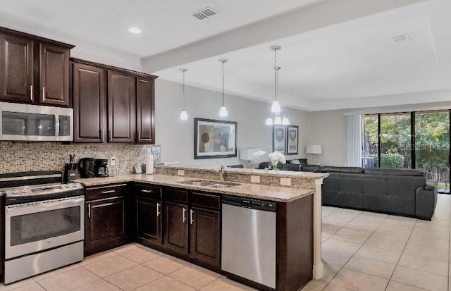 kitchen featuring stainless steel appliances, hanging light fixtures, open floor plan, a sink, and a peninsula