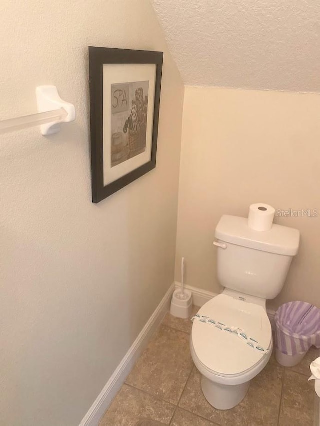 half bathroom with a textured ceiling, lofted ceiling, toilet, and baseboards