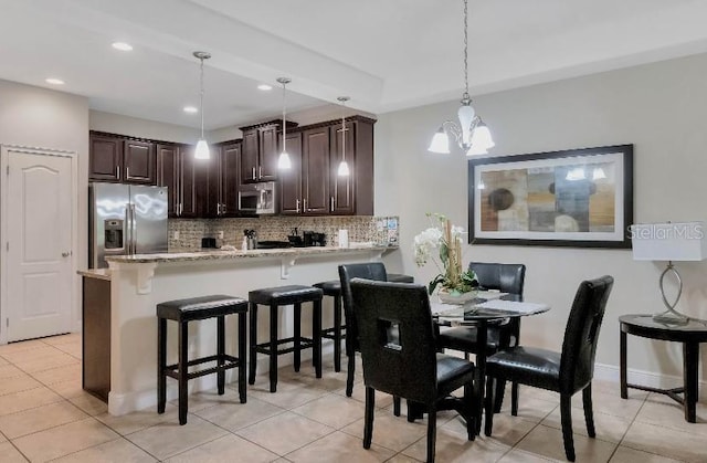 kitchen featuring a breakfast bar area, a peninsula, appliances with stainless steel finishes, tasteful backsplash, and decorative light fixtures