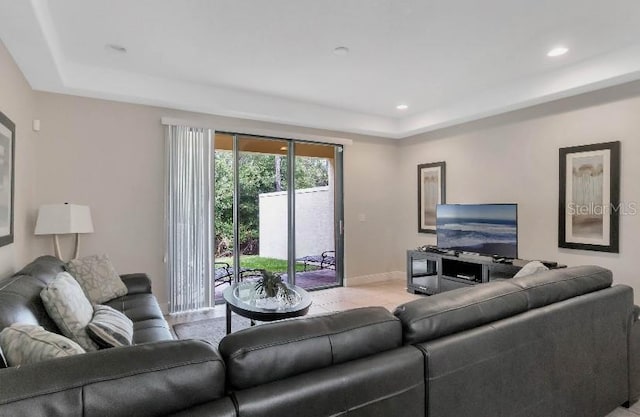 living room featuring a tray ceiling, recessed lighting, and baseboards