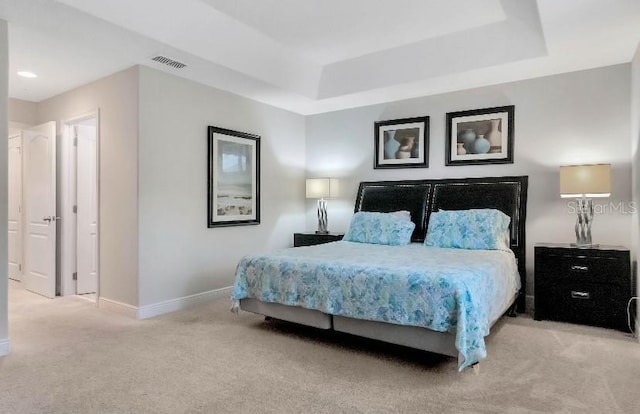 bedroom featuring baseboards, visible vents, a tray ceiling, and light colored carpet