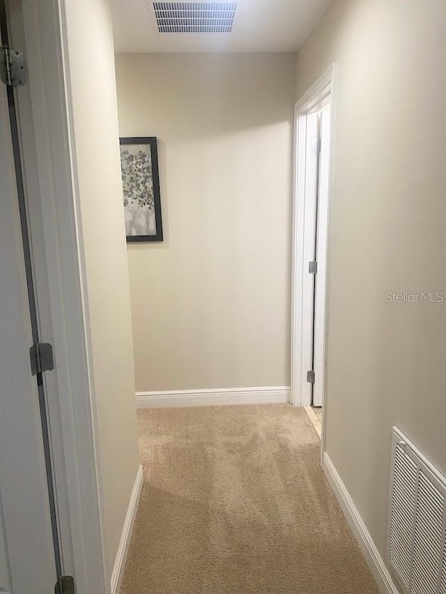 hallway with baseboards, visible vents, and light colored carpet