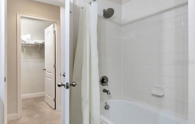 full bathroom featuring a spacious closet, shower / bath combo, and baseboards