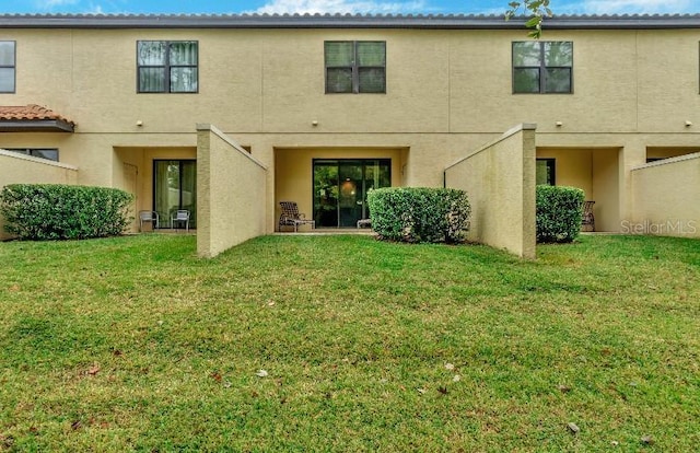 rear view of property featuring a lawn and stucco siding