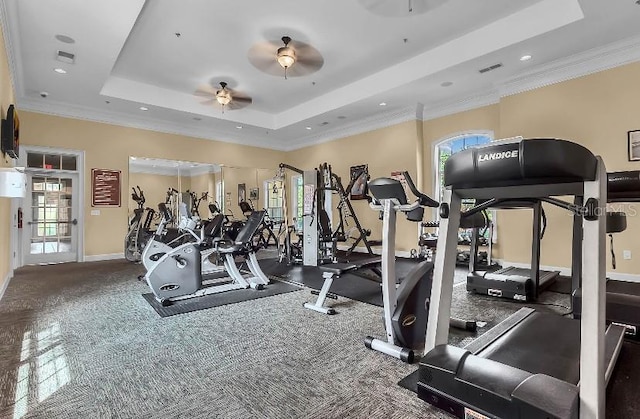 workout area featuring visible vents, a ceiling fan, baseboards, a tray ceiling, and crown molding