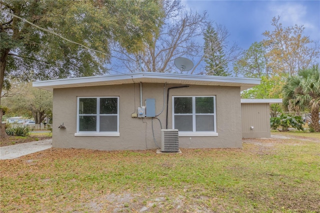 rear view of property with central AC, a lawn, and stucco siding