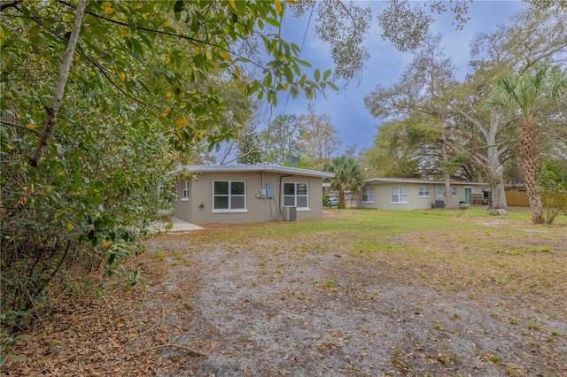 back of property featuring stucco siding, central AC unit, and a yard