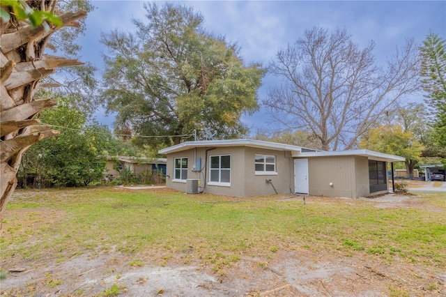 rear view of property featuring central air condition unit, a sunroom, and a lawn