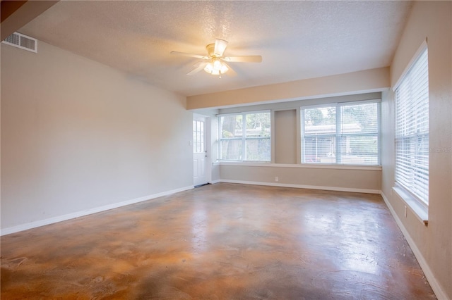 empty room with a textured ceiling, ceiling fan, visible vents, baseboards, and finished concrete floors