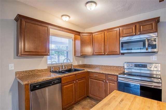 kitchen with brown cabinetry, stainless steel appliances, a textured ceiling, wooden counters, and a sink