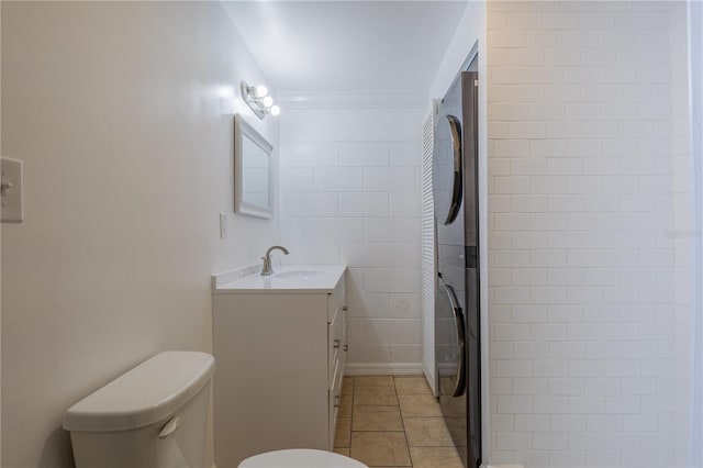 full bathroom featuring stacked washer / dryer, toilet, tile patterned flooring, crown molding, and vanity