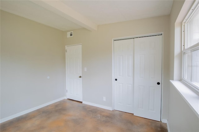 unfurnished bedroom with concrete flooring, visible vents, baseboards, a closet, and beamed ceiling