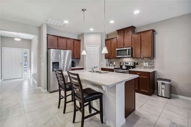 kitchen with sink, a breakfast bar area, appliances with stainless steel finishes, a kitchen island with sink, and backsplash