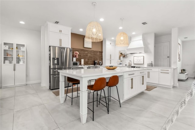 kitchen featuring appliances with stainless steel finishes, a kitchen bar, custom exhaust hood, hanging light fixtures, and a center island