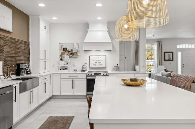 kitchen with white cabinetry, appliances with stainless steel finishes, decorative light fixtures, and custom range hood