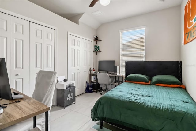 bedroom with multiple closets, vaulted ceiling, light tile patterned floors, and ceiling fan