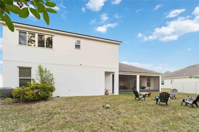 rear view of house featuring a yard, a sunroom, and an outdoor fire pit