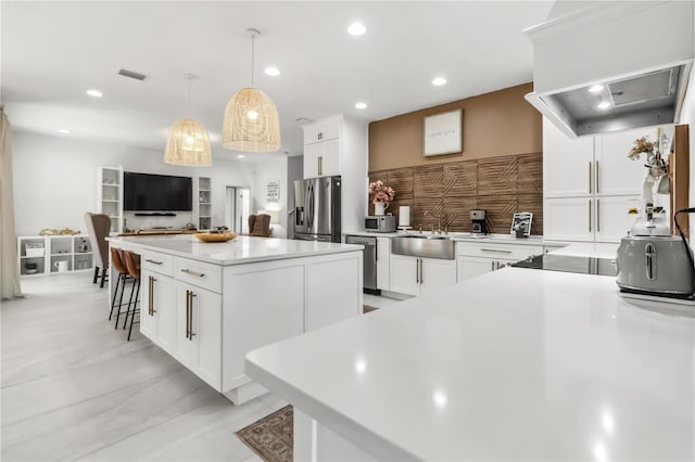 kitchen with decorative light fixtures, sink, white cabinets, stainless steel appliances, and a spacious island