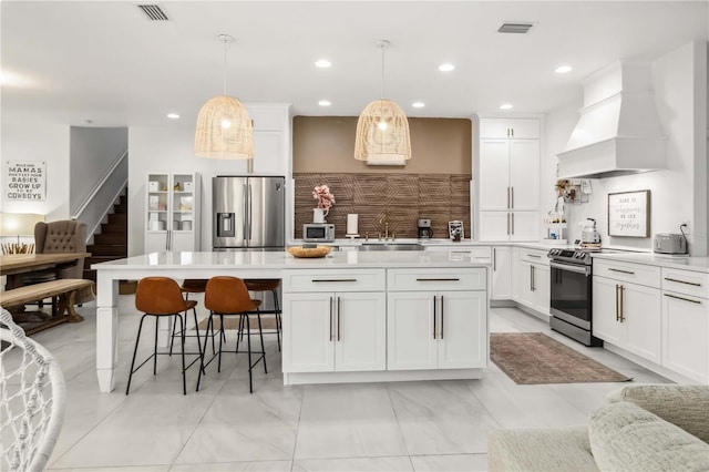 kitchen with pendant lighting, sink, premium range hood, appliances with stainless steel finishes, and a center island