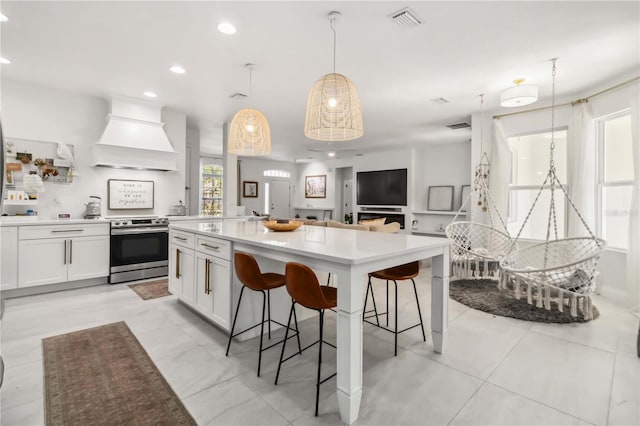 kitchen with premium range hood, pendant lighting, a breakfast bar area, white cabinets, and stainless steel range with electric stovetop