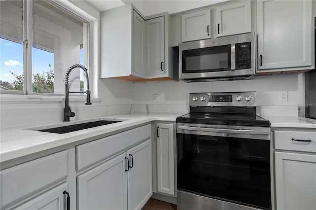 kitchen with light stone countertops, appliances with stainless steel finishes, sink, and gray cabinetry