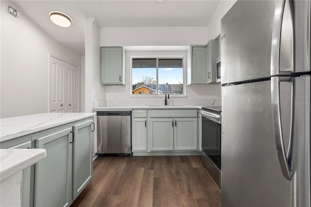 kitchen with sink, gray cabinets, appliances with stainless steel finishes, dark hardwood / wood-style floors, and light stone counters