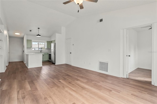 unfurnished living room featuring ceiling fan, lofted ceiling, sink, and light hardwood / wood-style flooring