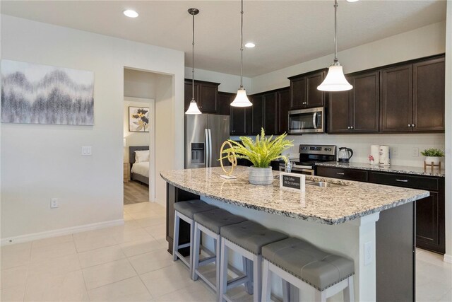 8896 Bengal Ct, Kissimmee, FL 34747 - kitchen featuring appliances with stainless steel finishes, a kitchen island with sink, hanging light fixtures, dark brown cabinets, and tasteful backsplash