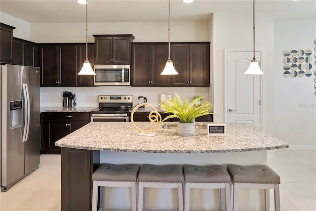 8896 Bengal Ct, Kissimmee, FL 34747 - kitchen featuring appliances with stainless steel finishes, decorative light fixtures, light stone countertops, and a kitchen island with sink