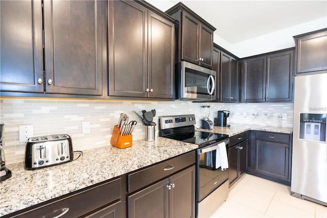 kitchen with tasteful backsplash, dark brown cabinetry, stainless steel appliances, and light stone countertops