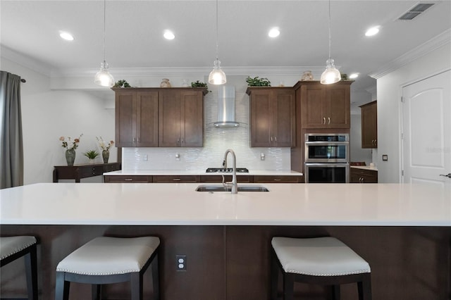 kitchen with wall chimney range hood, pendant lighting, and a large island with sink