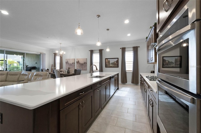 kitchen with sink, a kitchen island with sink, dark brown cabinets, stainless steel appliances, and decorative light fixtures