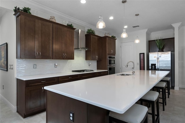 kitchen featuring sink, hanging light fixtures, a kitchen island with sink, dark brown cabinetry, and wall chimney range hood