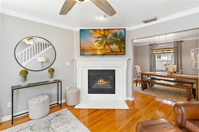 living room featuring crown molding, ceiling fan, a tile fireplace, and light wood-type flooring