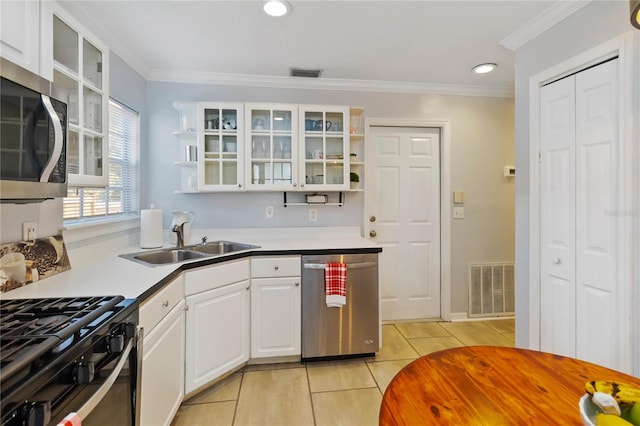 kitchen with appliances with stainless steel finishes, sink, white cabinets, ornamental molding, and light tile patterned floors